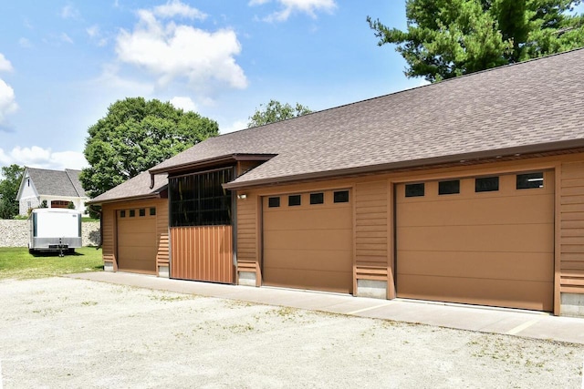 view of front facade featuring an outdoor structure, a garage, and roof with shingles