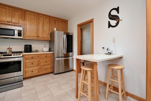 kitchen with brown cabinetry, a breakfast bar, light tile patterned flooring, light countertops, and appliances with stainless steel finishes