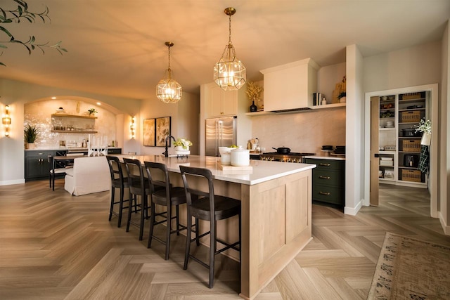 kitchen with decorative light fixtures, high end refrigerator, a kitchen island with sink, and parquet flooring