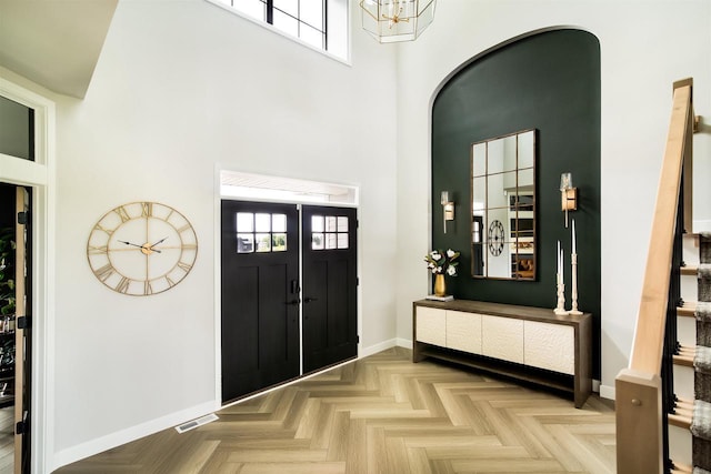 foyer entrance featuring a wealth of natural light, light parquet floors, a high ceiling, and a notable chandelier