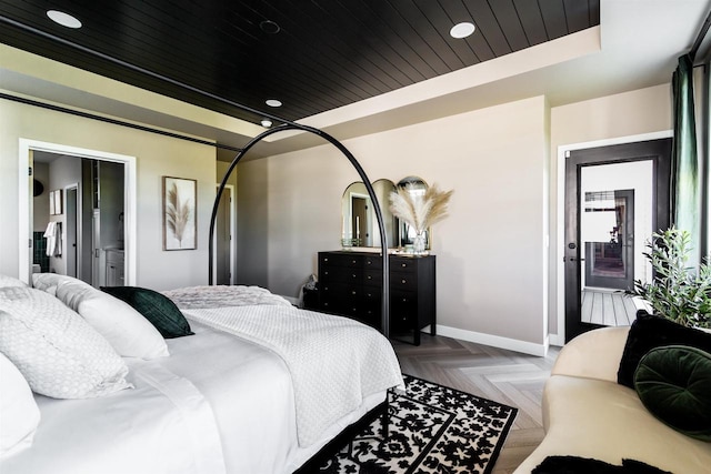 bedroom with a tray ceiling, light parquet flooring, ensuite bath, and wood ceiling