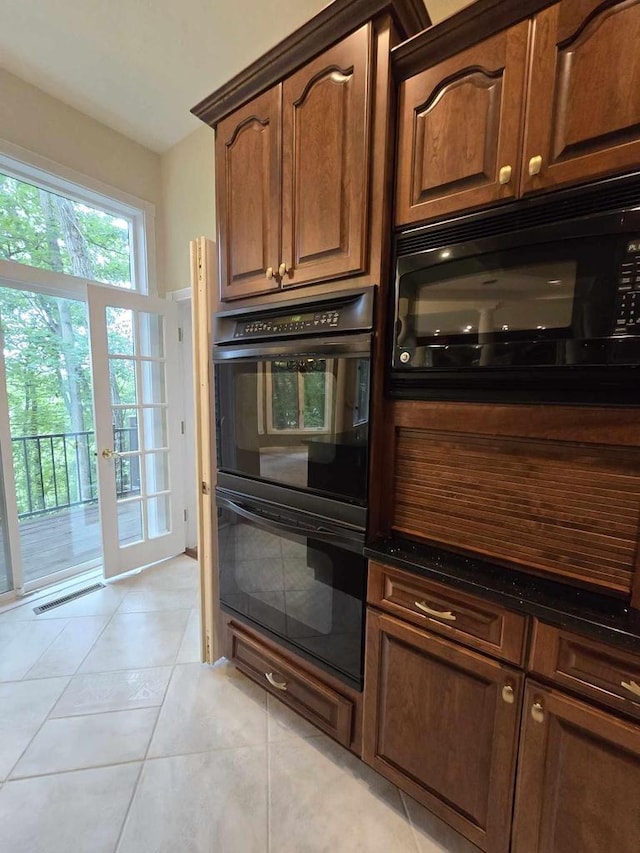 kitchen featuring light tile patterned floors, black appliances, and dark stone counters