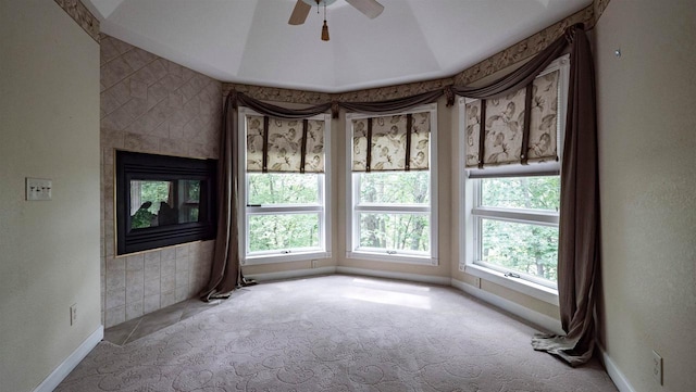 carpeted empty room featuring lofted ceiling, a tile fireplace, a raised ceiling, and a healthy amount of sunlight