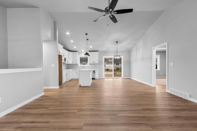 unfurnished living room with ceiling fan with notable chandelier, high vaulted ceiling, and light hardwood / wood-style flooring