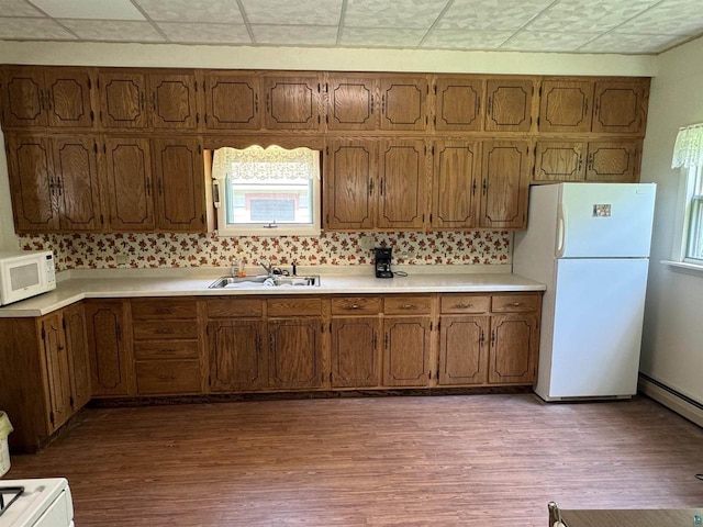 kitchen with sink, a baseboard heating unit, backsplash, light hardwood / wood-style floors, and white appliances