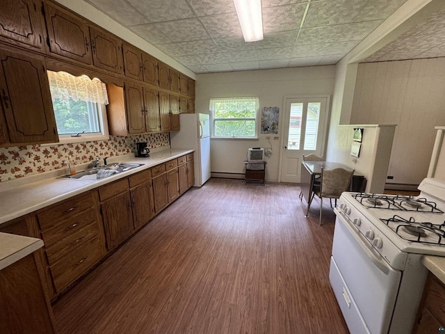 kitchen with sink, baseboard heating, dark hardwood / wood-style flooring, backsplash, and white appliances