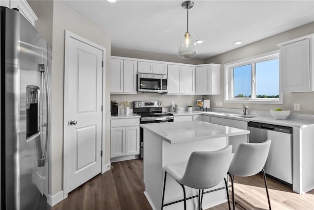 kitchen with white cabinetry, dark wood-type flooring, hanging light fixtures, stainless steel appliances, and a kitchen island