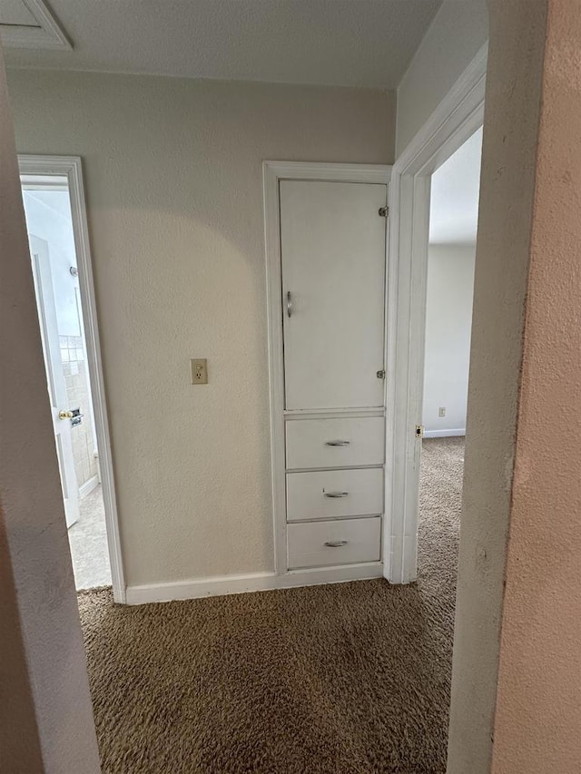 corridor featuring carpet, a textured wall, and baseboards