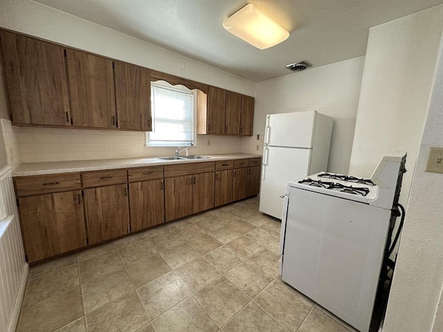 kitchen featuring white appliances, backsplash, a sink, and light countertops