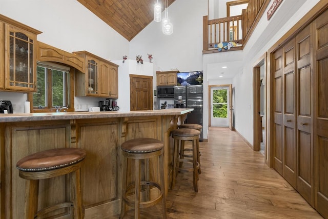 kitchen with black refrigerator, a kitchen breakfast bar, light wood-type flooring, a wealth of natural light, and high vaulted ceiling