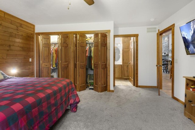 bedroom with ensuite bath, ceiling fan, wood walls, a walk in closet, and light carpet