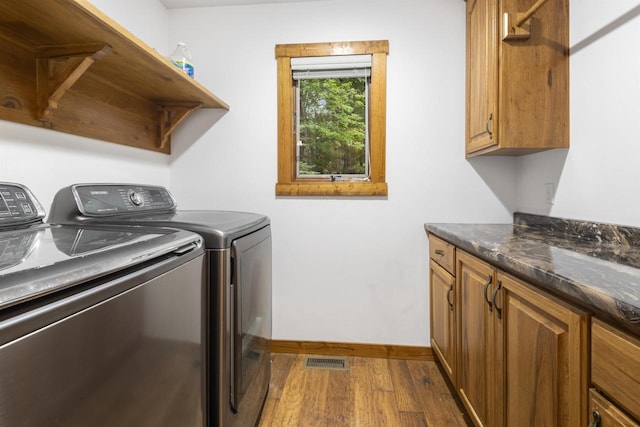 clothes washing area featuring cabinets, hardwood / wood-style flooring, and washing machine and clothes dryer