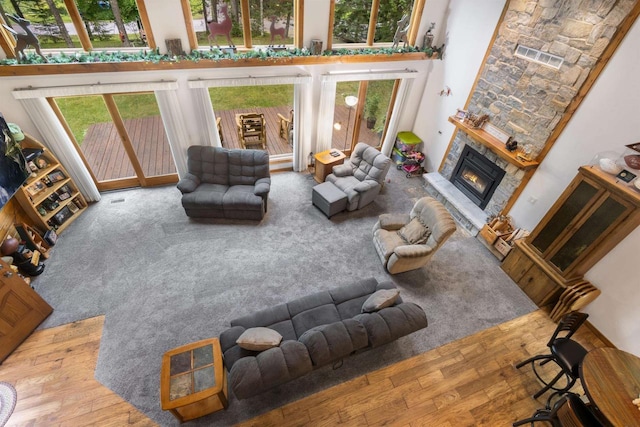 living room with a stone fireplace, wood-type flooring, and a high ceiling