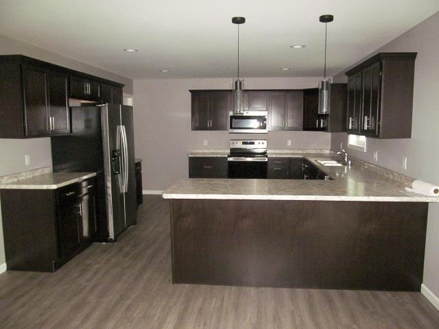 kitchen with dark brown cabinetry, hanging light fixtures, stainless steel appliances, kitchen peninsula, and hardwood / wood-style floors