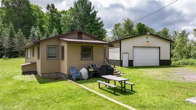 rear view of property with a garage, a yard, and an outbuilding