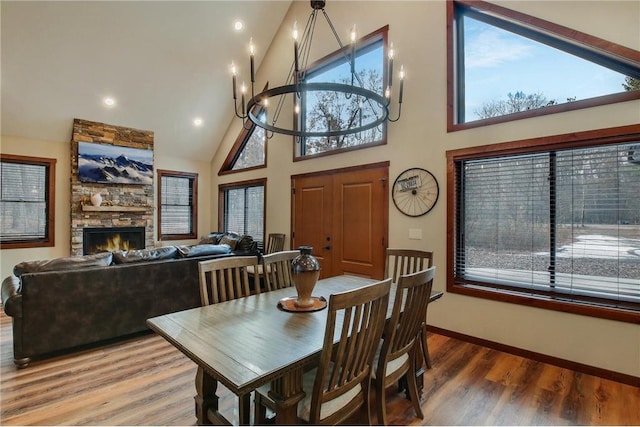 dining space featuring wood-type flooring, a fireplace, high vaulted ceiling, and a chandelier