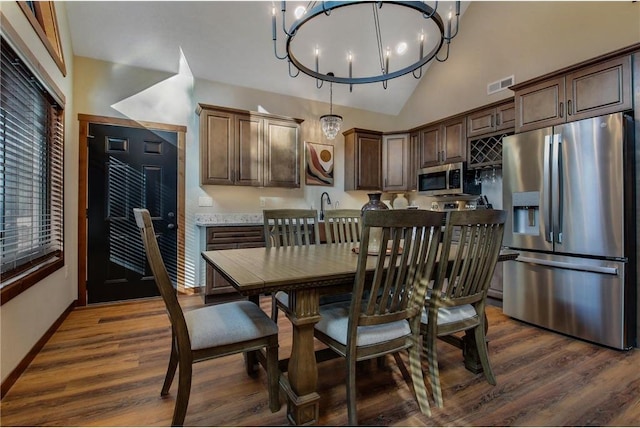 dining space with sink, high vaulted ceiling, dark wood-type flooring, and an inviting chandelier