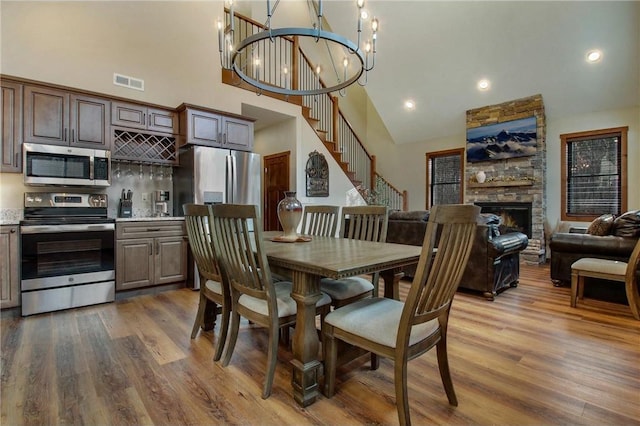 dining area featuring a stone fireplace, wood-type flooring, high vaulted ceiling, and an inviting chandelier