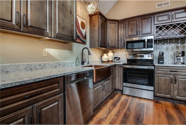 kitchen with stainless steel appliances, light stone counters, dark wood-type flooring, and sink