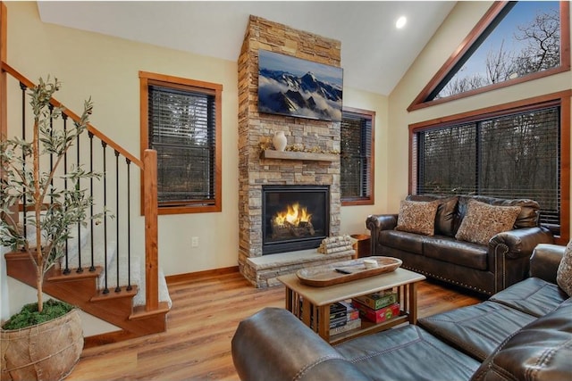 living room with a stone fireplace, light hardwood / wood-style flooring, and vaulted ceiling