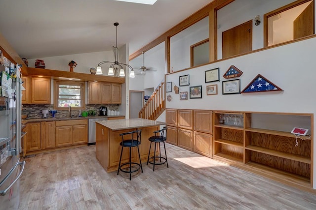 kitchen featuring a center island, hanging light fixtures, tasteful backsplash, stainless steel dishwasher, and light wood-type flooring