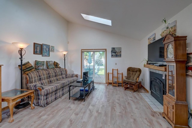 living room featuring a skylight, light hardwood / wood-style flooring, a tile fireplace, and high vaulted ceiling