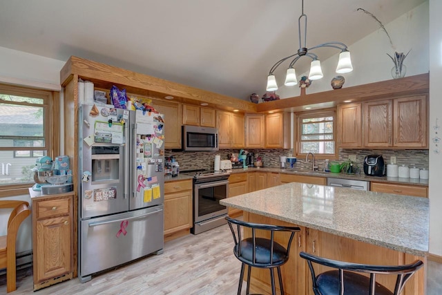 kitchen featuring light stone countertops, sink, stainless steel appliances, light hardwood / wood-style flooring, and decorative light fixtures