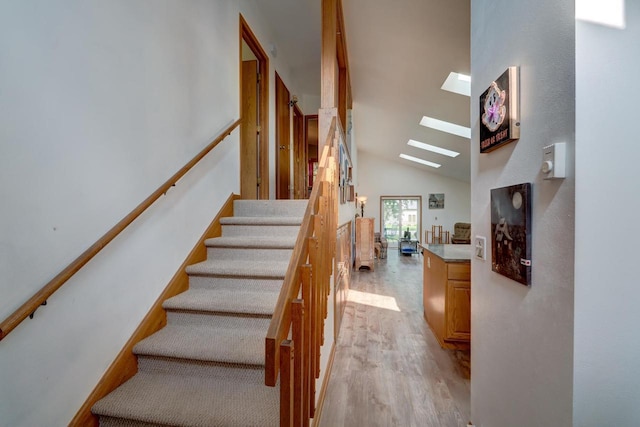 stairs with wood-type flooring, a skylight, and high vaulted ceiling