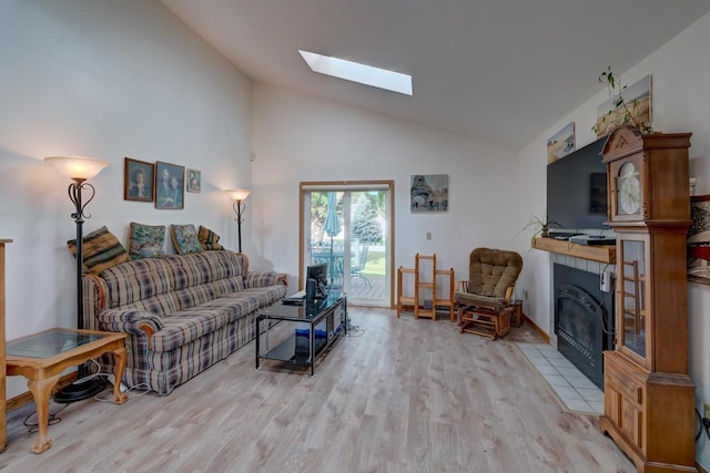 living room with a skylight, a fireplace, high vaulted ceiling, and light wood-type flooring