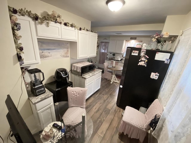 kitchen with dark hardwood / wood-style flooring, white cabinetry, black fridge, and light stone counters