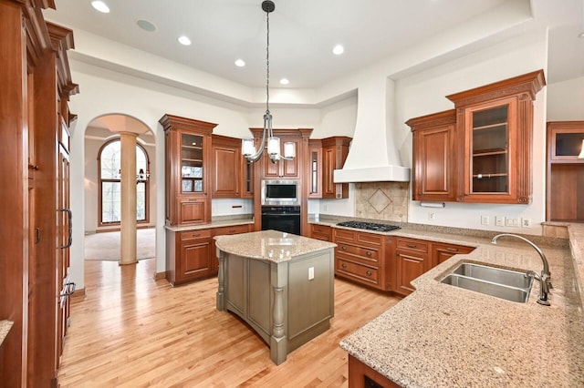 kitchen with custom range hood, stainless steel appliances, sink, pendant lighting, and a kitchen island