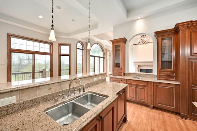 kitchen with a raised ceiling, decorative light fixtures, light stone counters, and sink