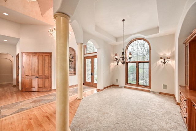 carpeted foyer entrance with a raised ceiling, ornate columns, french doors, and an inviting chandelier