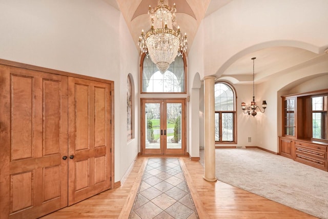 foyer entrance with a chandelier, french doors, decorative columns, and light hardwood / wood-style floors