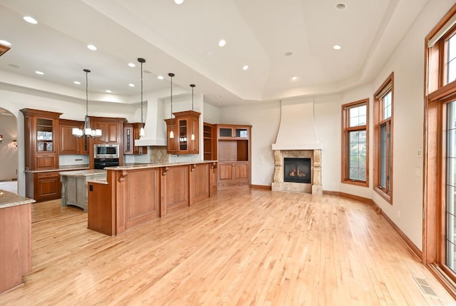 kitchen with stainless steel microwave, premium range hood, hanging light fixtures, a fireplace, and black oven