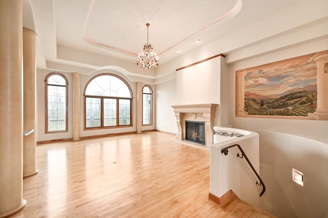 unfurnished living room with a healthy amount of sunlight, an inviting chandelier, light wood-type flooring, and a tray ceiling