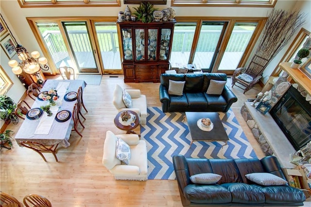 living room with a chandelier, a stone fireplace, a high ceiling, and light hardwood / wood-style flooring