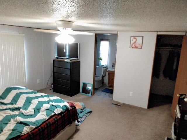 carpeted bedroom featuring ensuite bathroom, a walk in closet, ceiling fan, a textured ceiling, and a closet