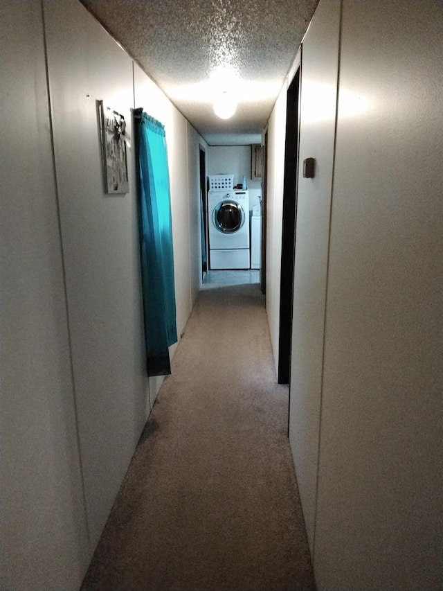 hall with a textured ceiling, washing machine and dryer, and light colored carpet