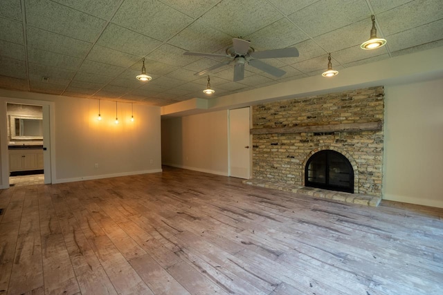 unfurnished living room featuring ceiling fan, a fireplace, a drop ceiling, and hardwood / wood-style flooring