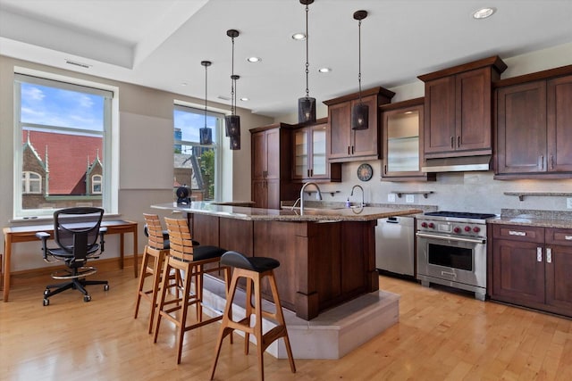 kitchen featuring light stone counters, a breakfast bar, stainless steel appliances, a center island with sink, and hanging light fixtures