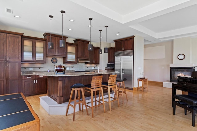 kitchen featuring light stone counters, pendant lighting, a kitchen island with sink, a breakfast bar, and appliances with stainless steel finishes