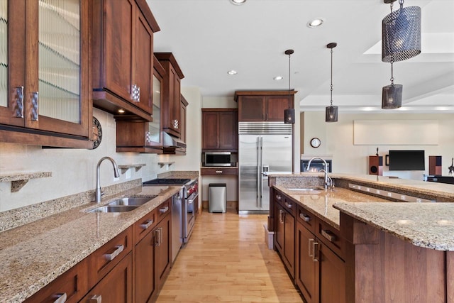 kitchen featuring light stone counters, high end appliances, sink, pendant lighting, and light hardwood / wood-style floors