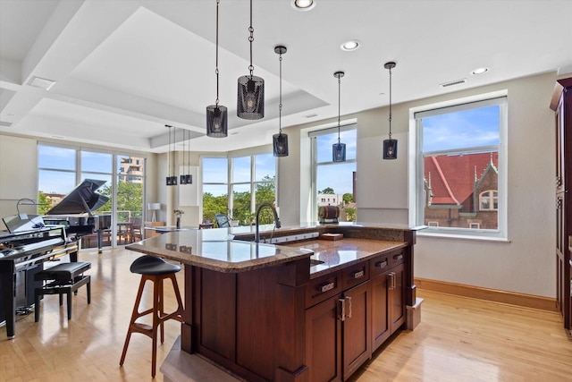 kitchen featuring light stone countertops, decorative light fixtures, a center island with sink, and light hardwood / wood-style floors