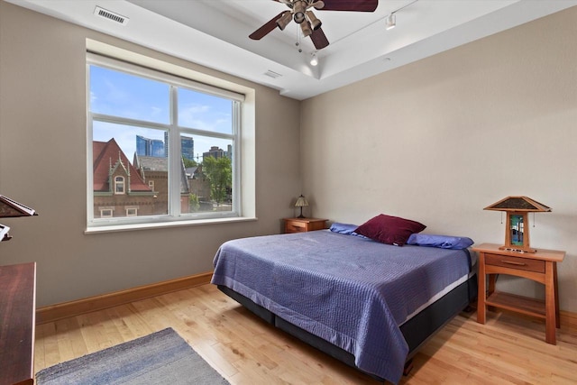 bedroom with light hardwood / wood-style floors, a raised ceiling, and ceiling fan