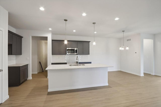 kitchen with light hardwood / wood-style flooring, tasteful backsplash, sink, and an island with sink