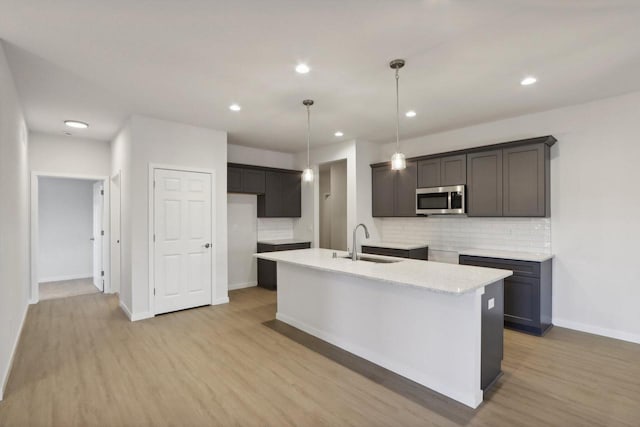 kitchen featuring decorative light fixtures, a center island with sink, tasteful backsplash, and light hardwood / wood-style floors