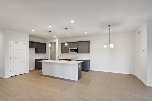 kitchen featuring decorative light fixtures, a center island with sink, and light hardwood / wood-style floors