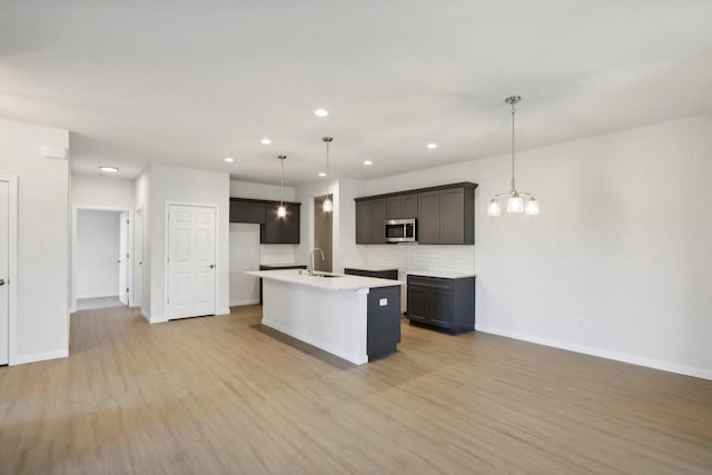 kitchen featuring decorative backsplash, light wood-type flooring, sink, hanging light fixtures, and an island with sink