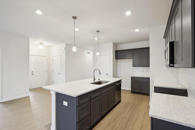 kitchen featuring a kitchen island with sink, sink, decorative backsplash, decorative light fixtures, and light hardwood / wood-style floors